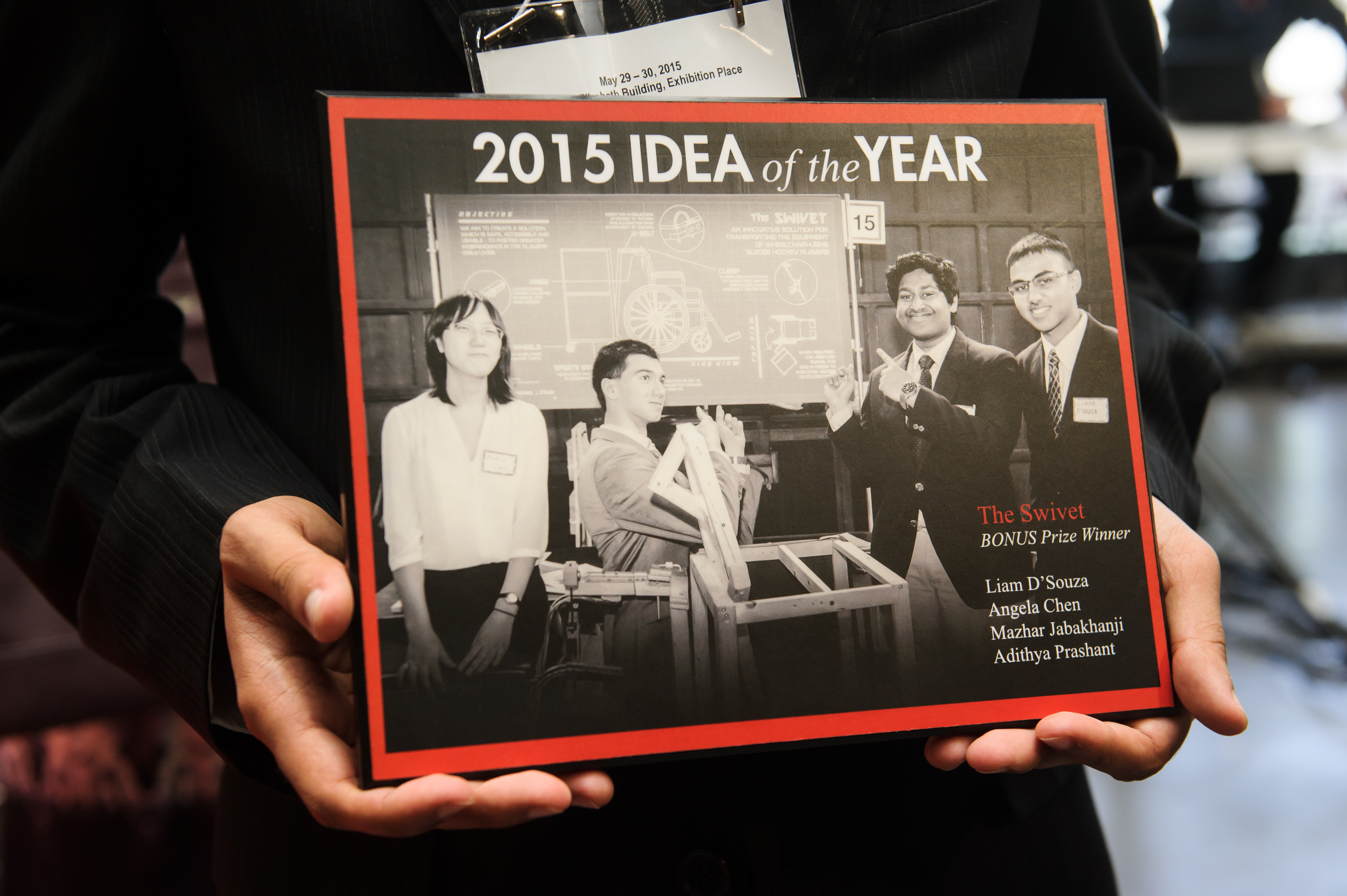 Someone holding the Swivet Team award for 2015 Idea of the Year with the team pointing to their poster and showing their product. Text Reads: 2015 Idea of the Year, The Swivet, Bonus Prize Winner, Liam D'Souza, Angela Chen, Mazhar Jabakhanji, Adithya Prashant