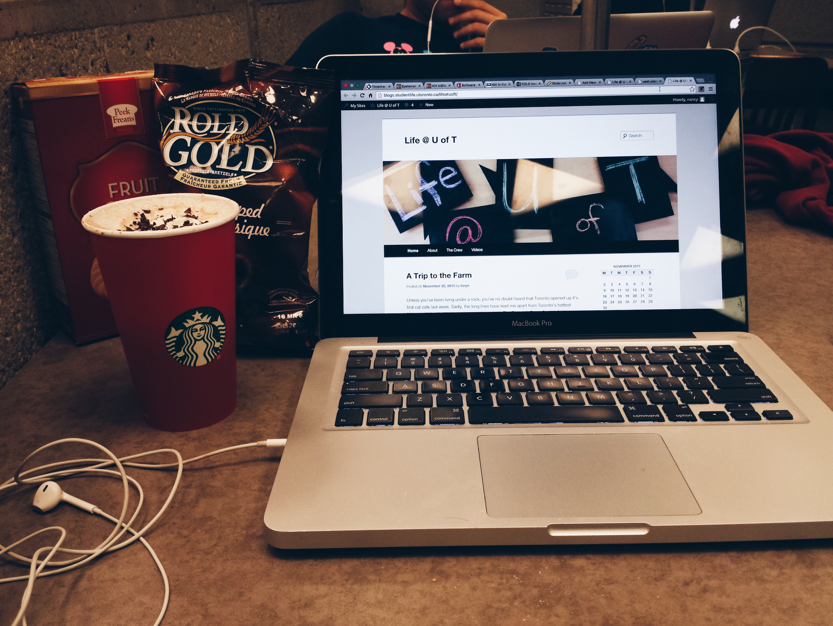 My laptop, earphones, a Starbucks cup, and a bag of Pretzals on a desk at Robarts.