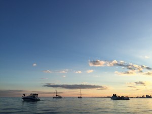 A photo of boats floating along lake ontario against the beginnings of a sunset