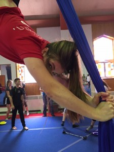 Annette is shown hanging upside down from aerial silks.