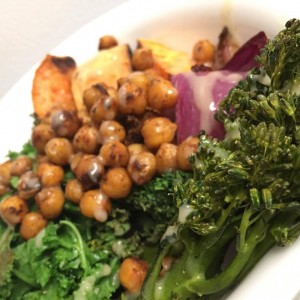 Bowl containing sweet potato, toasted chickpeas, red onion and kale drizzled with a sauce. 