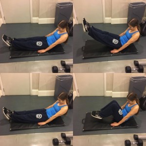 Annette demonstrates an abdominal exercise, holding a hollow position belly up on the floor with her legs extended then lifting her legs higher off the floor, lowering down and bringing them in towards her chest. 