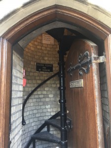a photo of an open wooden doorway that opens up to a black metal spiral staircase against a brick wall