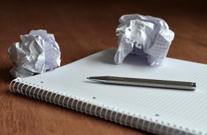 A picture of a notepad and pen with crumples balls of paper