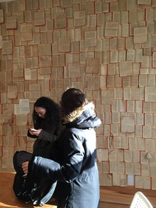 ALT="A room with a wall of book pages and two people getting ready to leave"