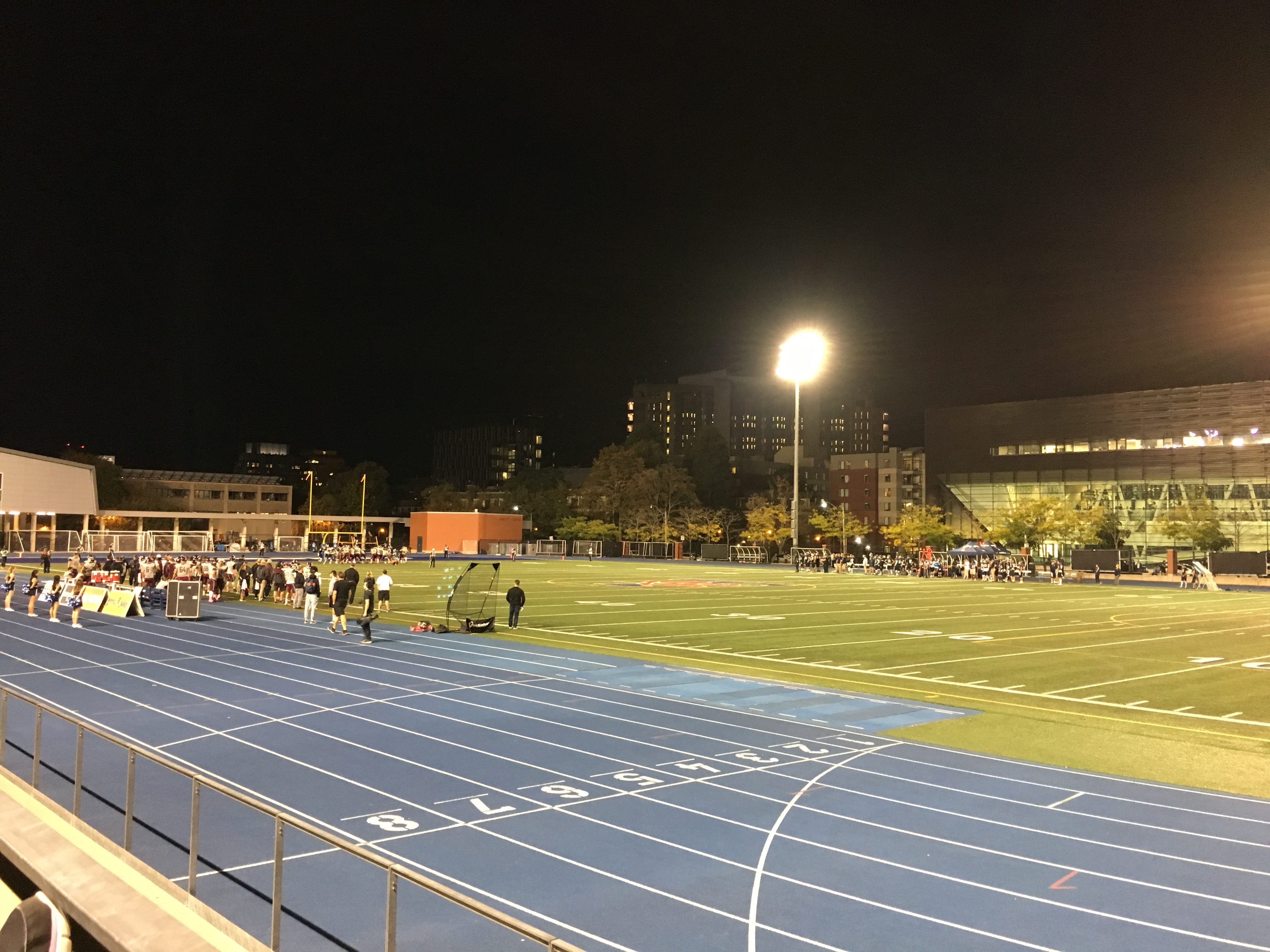 A football field at night, surrounded by a blue track. 