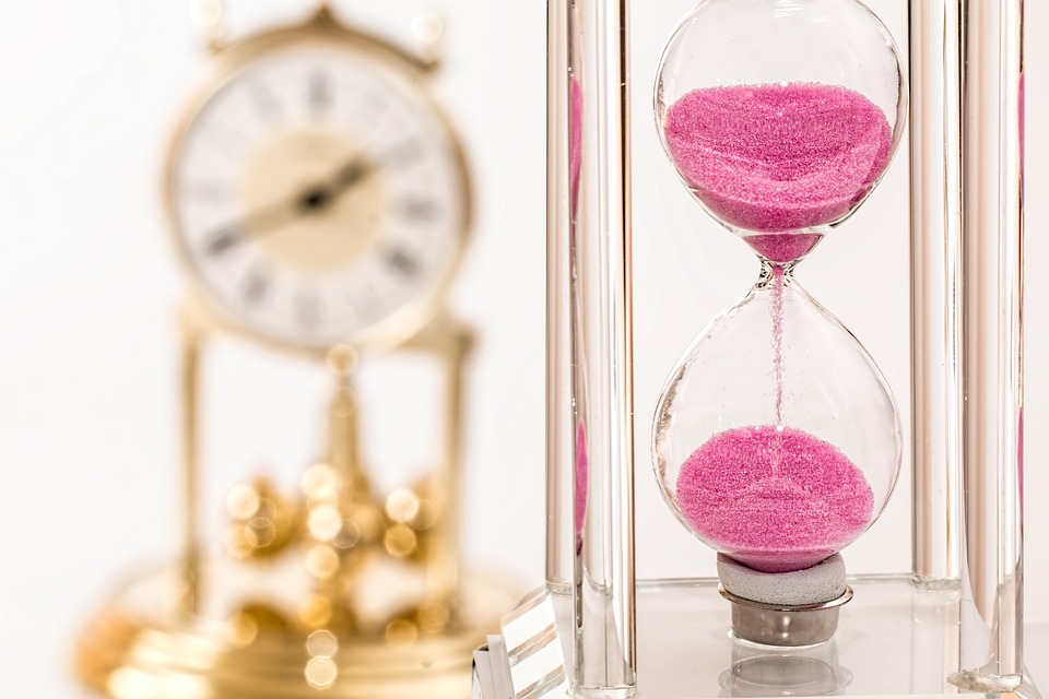 A pink hourglass and gold clock in the background