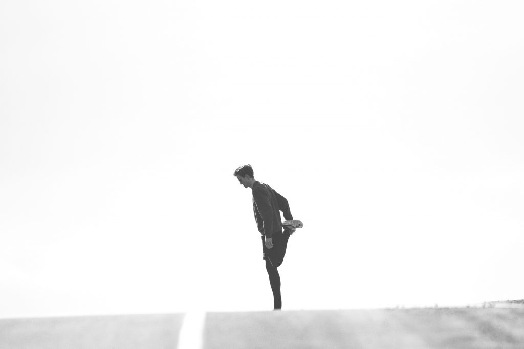 A man stretches his thigh before running on a black and white road.