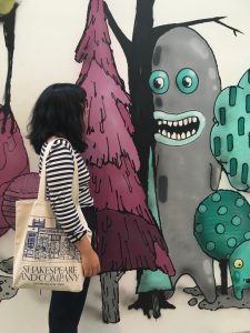 a photo of me positioned to look like I'm conversing with a cartoon of a friendly surreal oblong creature painted on the wall