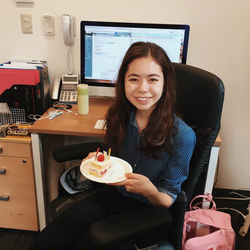 Emi sitting in office holding birthday cake.