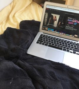 A computer displaying Netflix on a bed. 