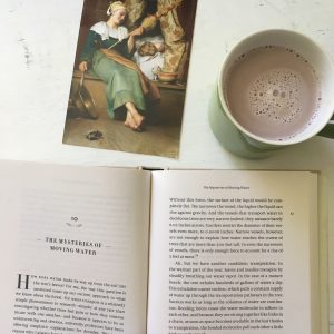 Postcard of a woman, a mug of hot chocolate, and an open book. 