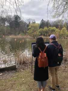 Two people, not facing the camera, standing by a pond