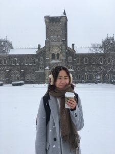 picture of me in front of the U of T main campus building in the winter, holding a cup 