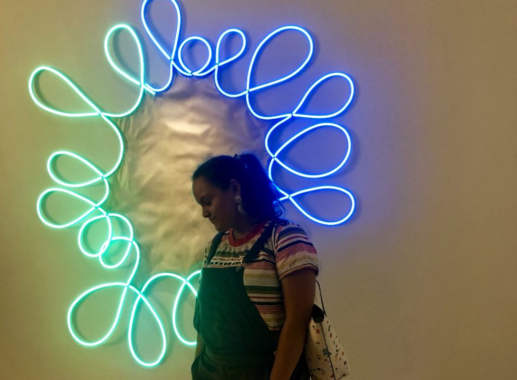 Francesca standing in front of a neon light piece by Brian Jungen at the AGO.