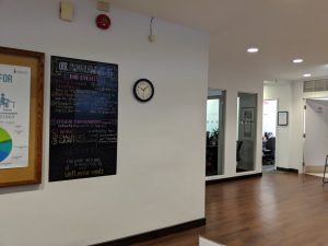 Bright office with hardwood floors, a clock on a wall, and some boards with information