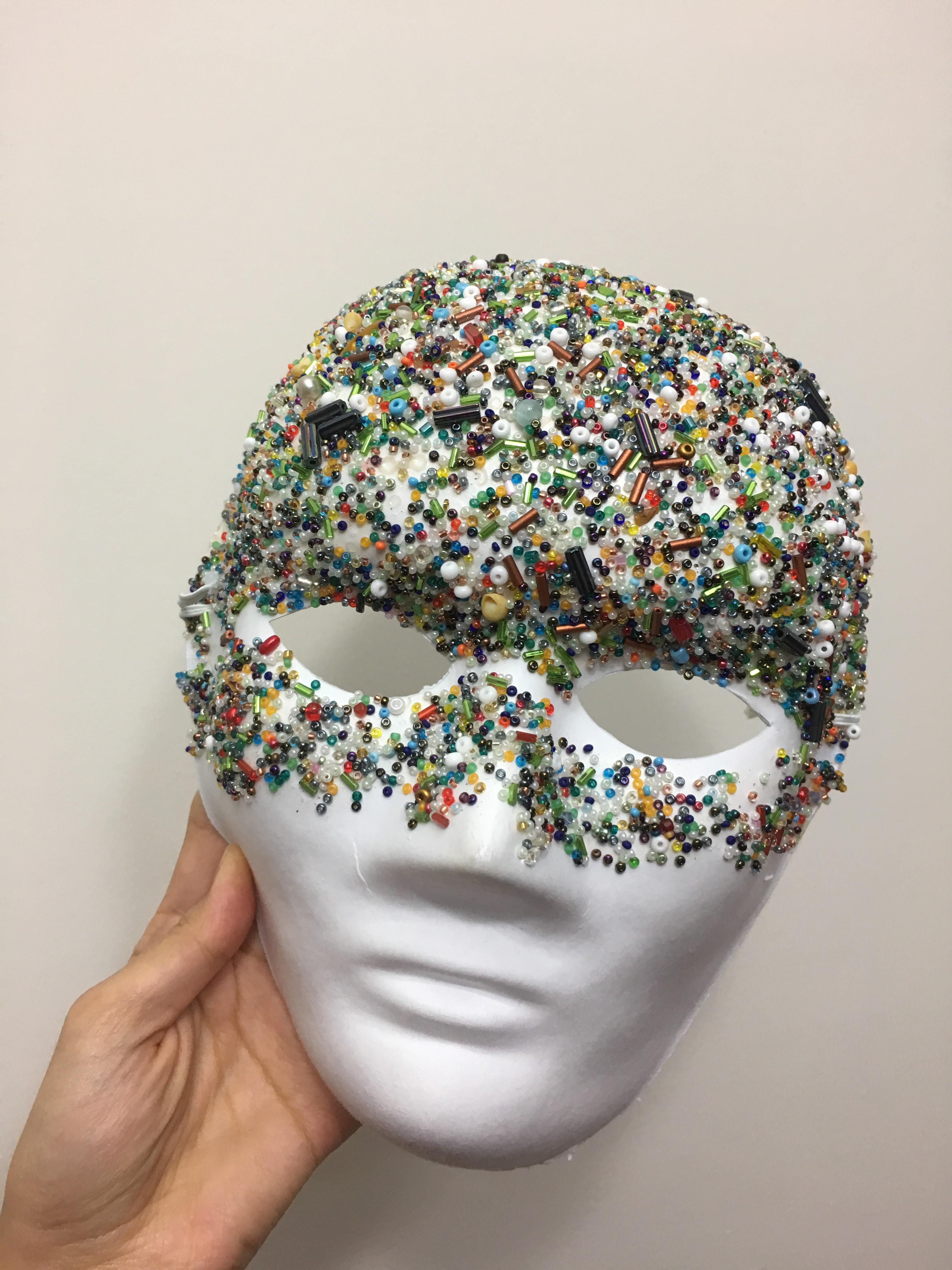 Picture of a white mask with beads glued to it 