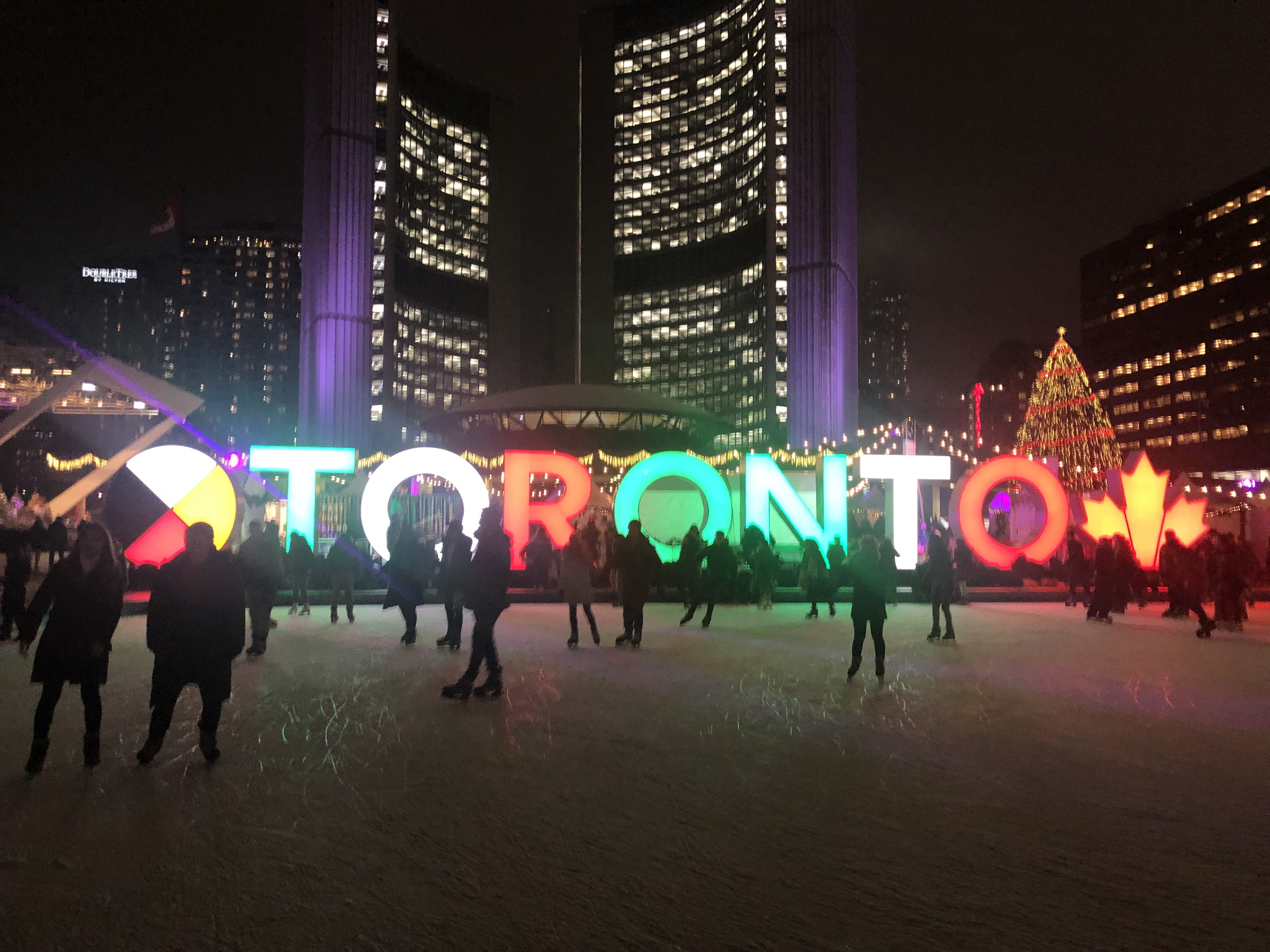 A picture of people ice skating in Nathan Phillips Square with the Toronto sign in the background lit up in different colours.
