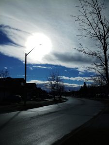 The sun shines through clouds on an empty street.
