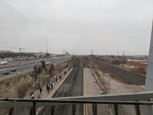 Photo from a bridge of train tracks, people waiting for a train, and a highway