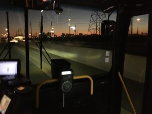 The sun sets on a dark skyline, as seen from inside a bus.