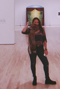 Francesca posing for a photograph in the National Art Gallery. She is wearing ripped jeans, a patterned shirt, and a patterned scarf of the same tones.
