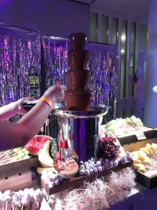 A chocolate fountain surrounded by fruits.