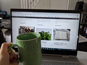 Green coffee cup held in front of a laptop open to various blog posts 