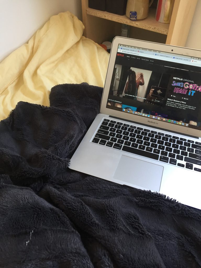 A picture of a computer with Netflix on the screen in a bed. 