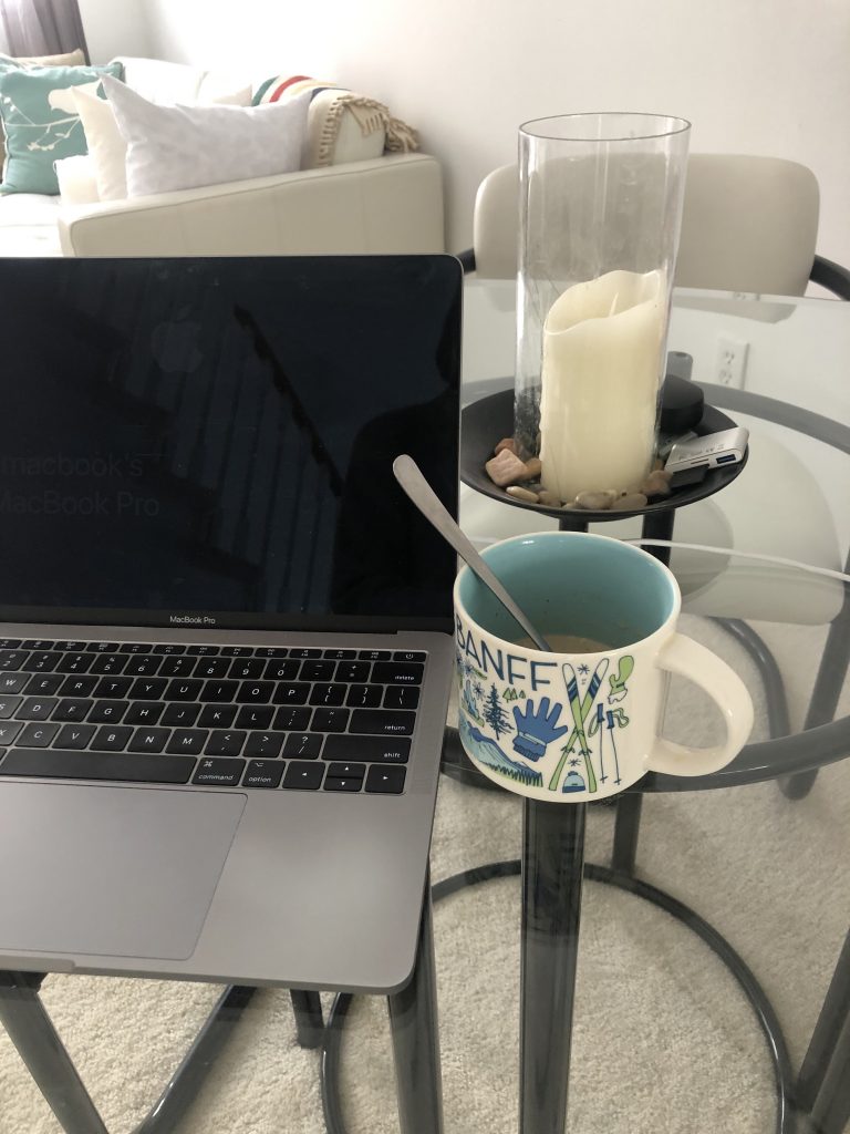 A mug of coffee sits beside a laptop on a glass table.