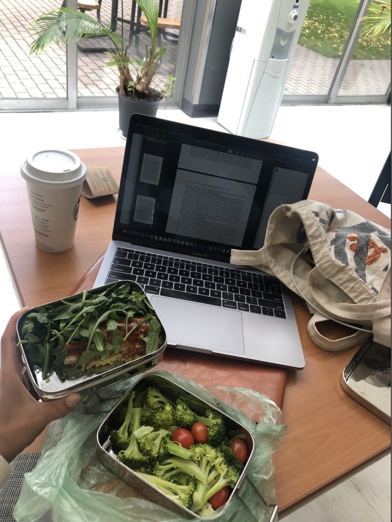 A boxed lunch of salad and rice along with a laptop and tote bag on a table.