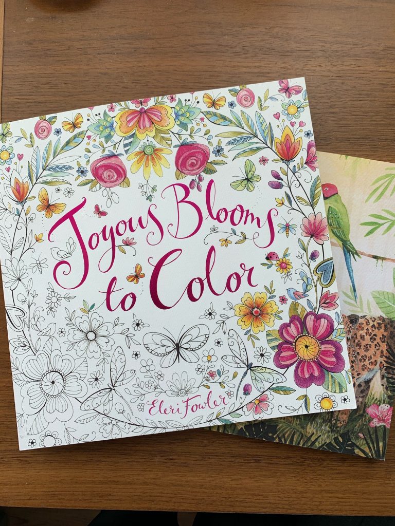 the coloring book "joyous bloom to color" on a brown desk background