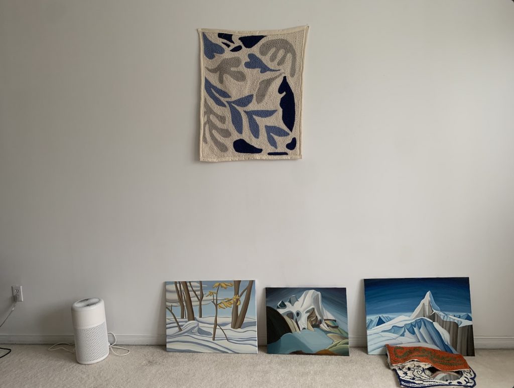 three paintings leaning against a wall, with a rug pinned on the wall