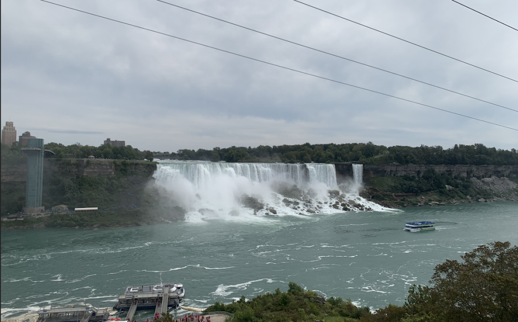 a photo of the Niagra Falls waterfall from the Canadian side. A boat is in the water below.