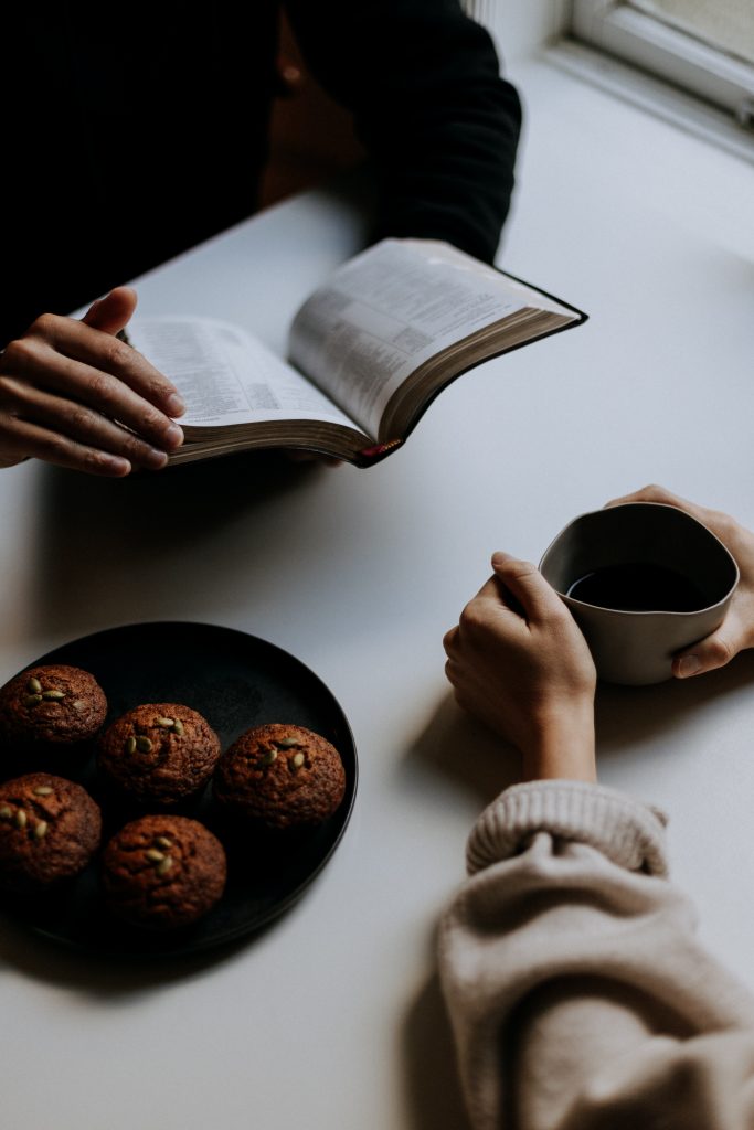 a table with Bible, a plate of muffins, and a cup of coffee