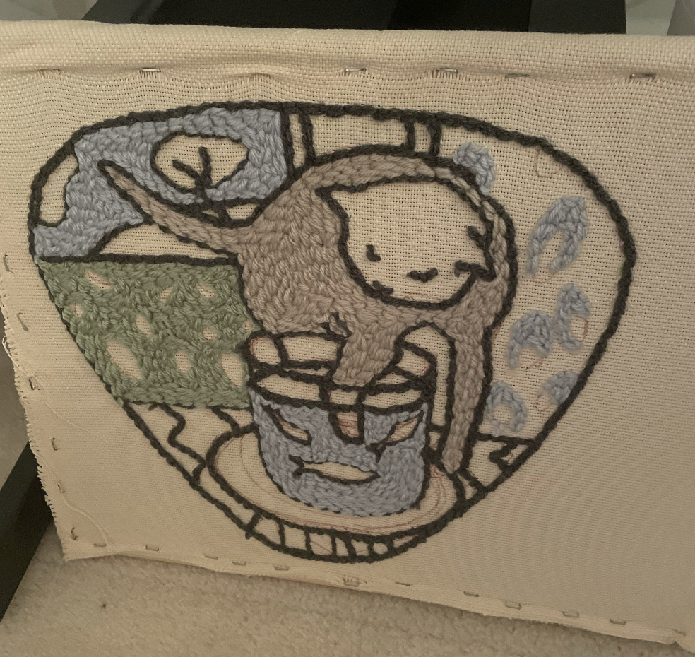 picture of incomplete embroidery of a cat dipping its paw into a glass of water