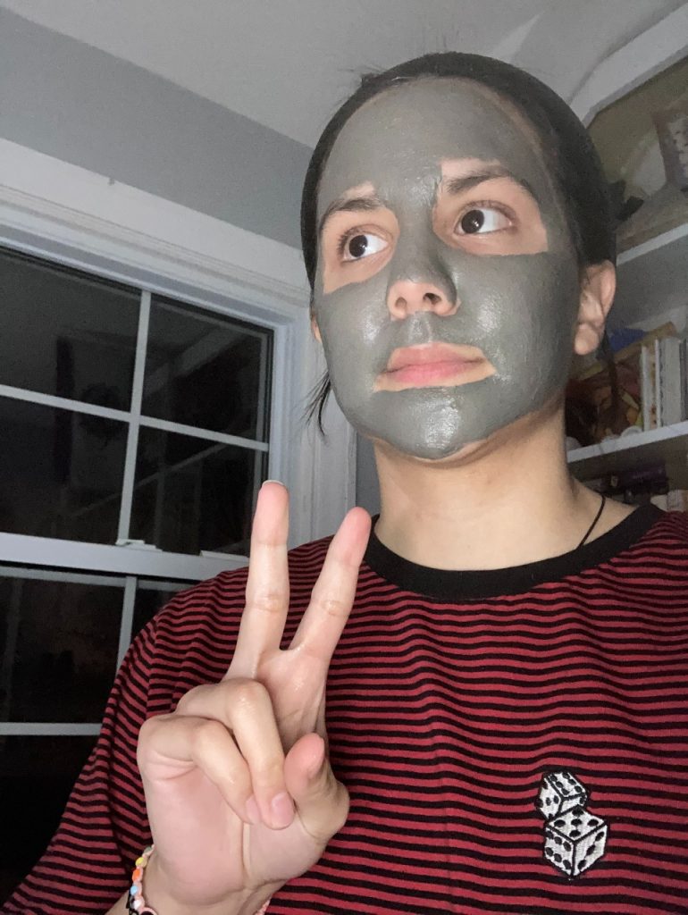 girl with facial mud mask holding a peace sign