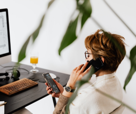 Person in front of their computer talking on the phone while looking at messages on a separate device 