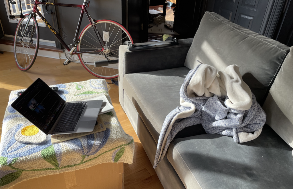 a crumpled blanket on a couch with a laptop on a cardboard box as a side table