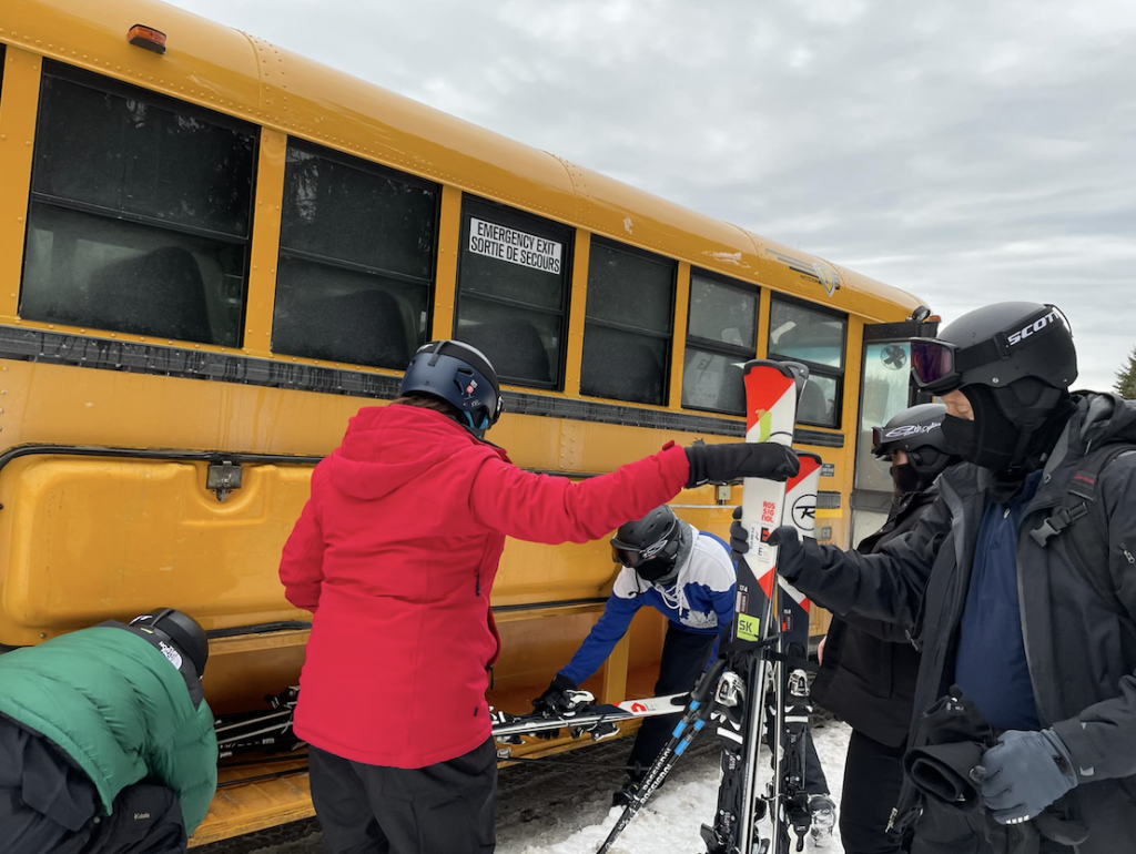 skiers loading skis into the storage of a yellow school bus