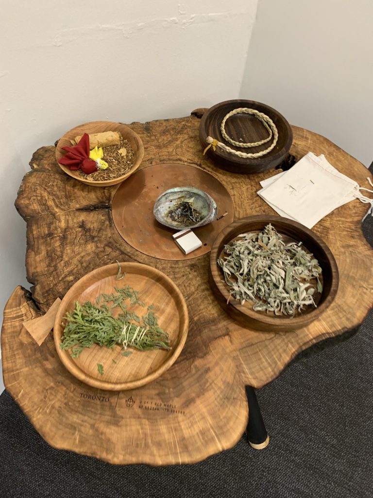 Wooden smudging table with 4 bowls of sage, cedar, sweetgrass and tobacco.