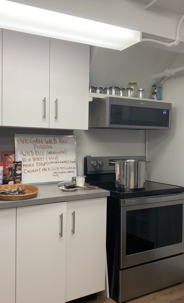 Kitchen with white cabinets, a black and silver oven with a whiteboard saying "Vegan Wild Rice Pudding"