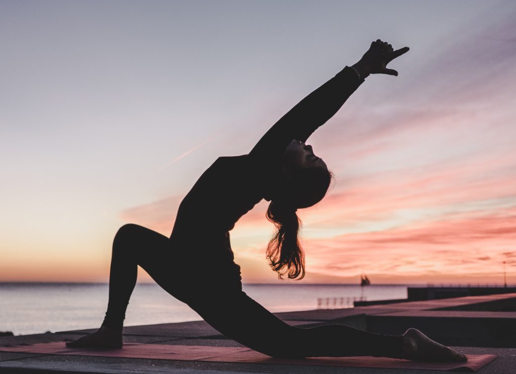 Person doing a yoga pose on a dock by water with a sunset in the background