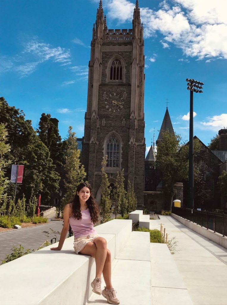Girl (Sammi) sitting in front of University College building on summer day.