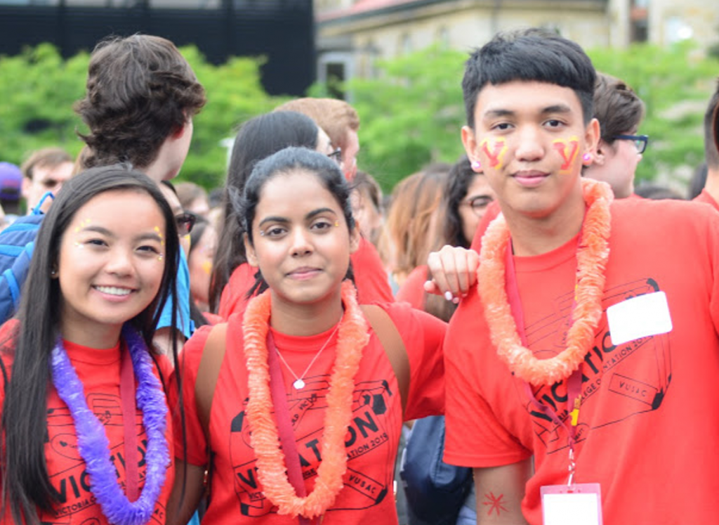 Three friends wearing red Victoria College t-shirts and leis.