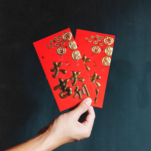 A hand holding two red envelopes with Chinese calligraphy. 