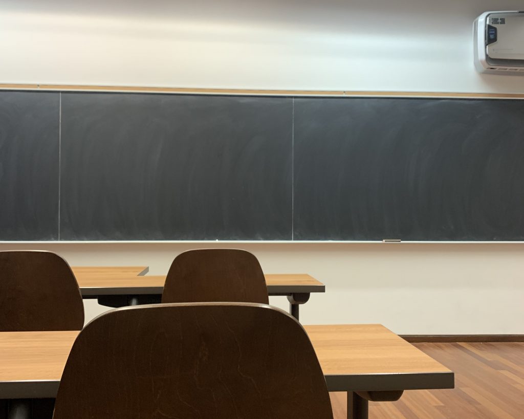 A classroom with black chalkboards and empty seats in front.