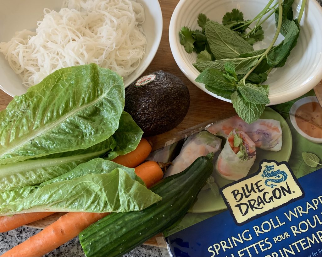 Ingredients laid out: rice noodles, lettuce, carrot, cucumber, avocado, mint leaves, and spring roll wrapper