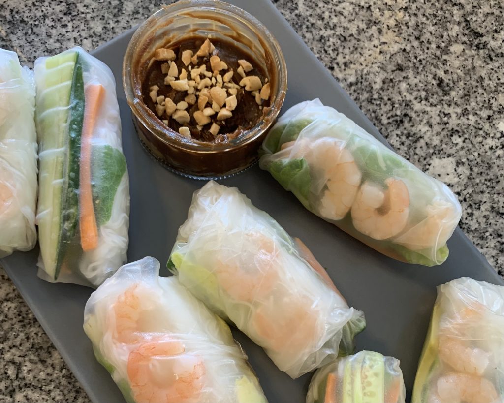 Summer rolls on a grey plate with a side of peanut sauce