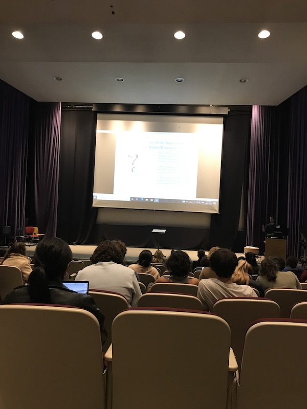 Photo of a lecture hall with students looking at a screen